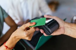 a hand holding a Point of Sale POS terminal while receiving a card payment from another hand